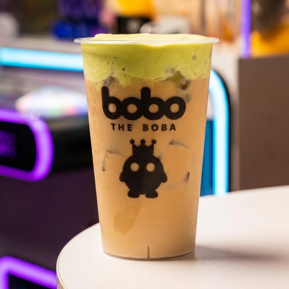 Boba The Boba drink with green foam on top, on a white table with neon lights in the background.