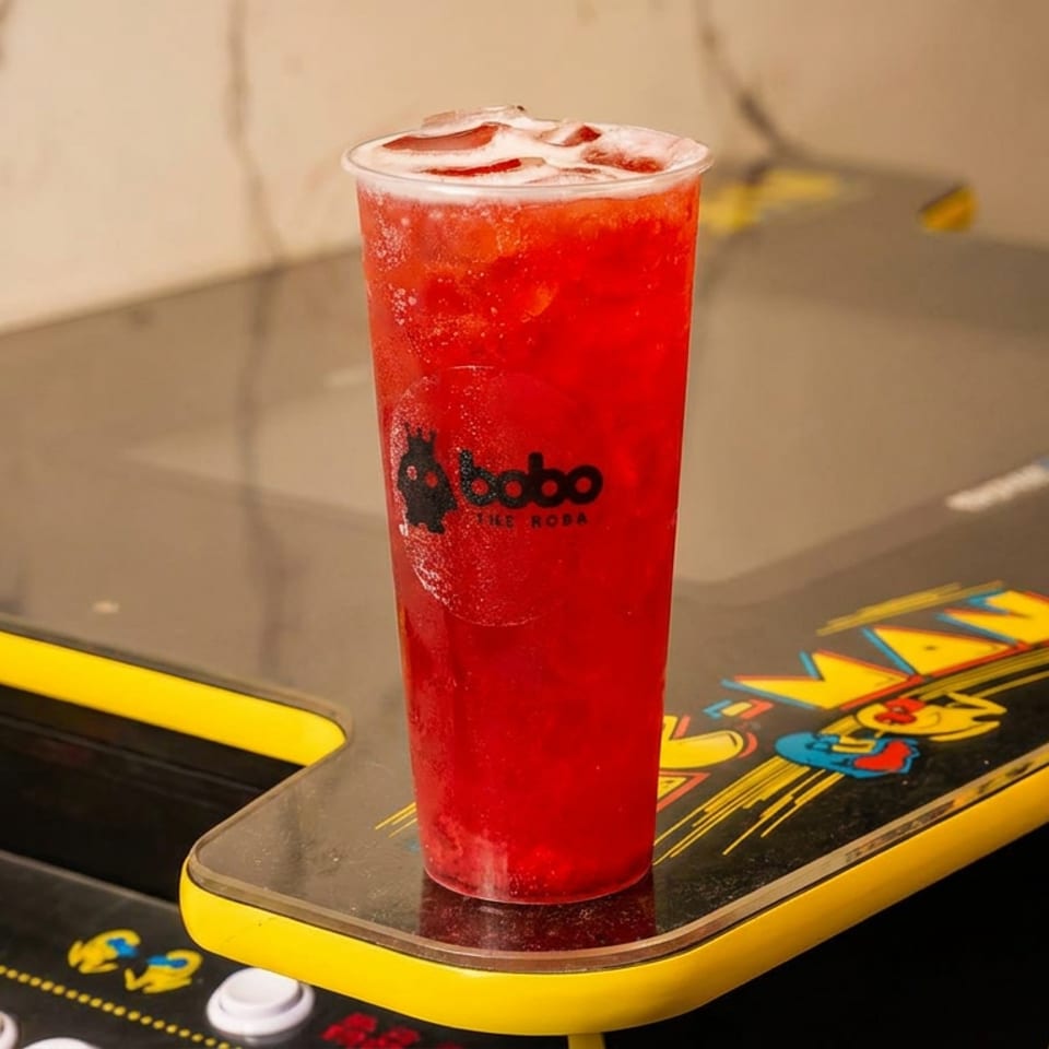 A red Boba drink with ice sits on a Pac-Man arcade game machine.