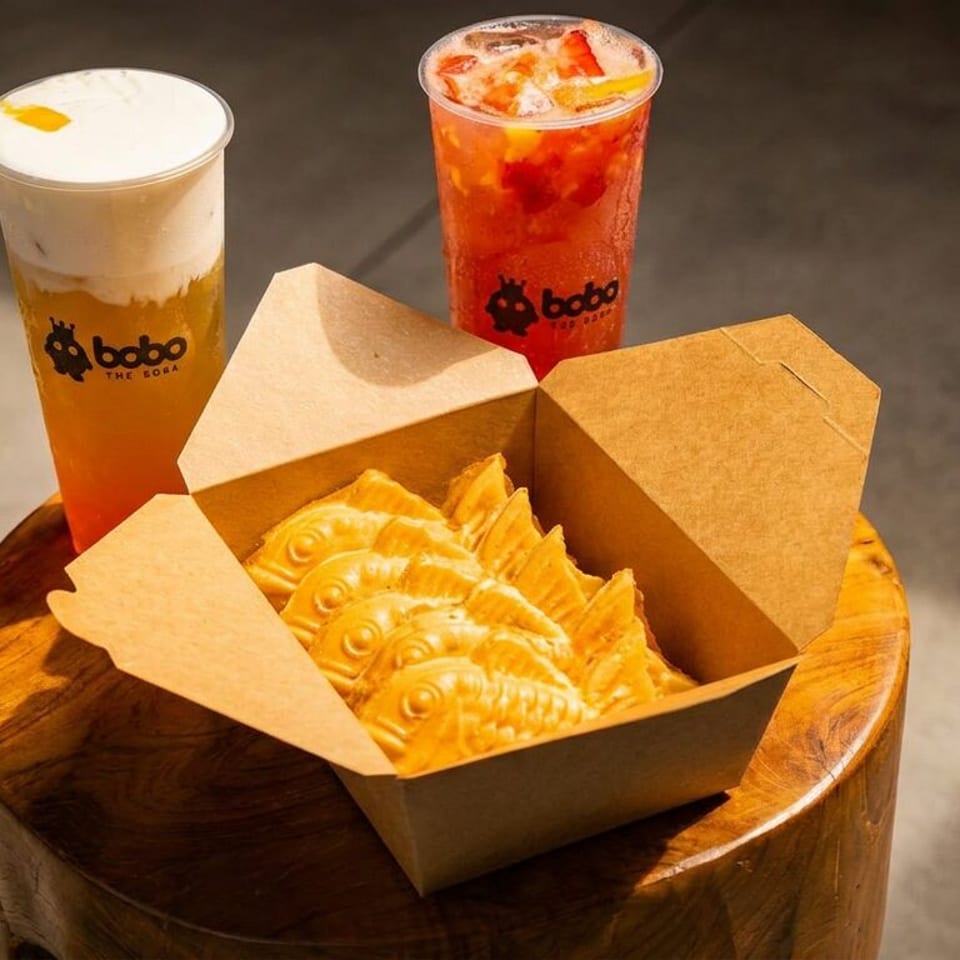 Two Bobo The Boba drinks and a box of taiyaki pastries on a wooden stool.