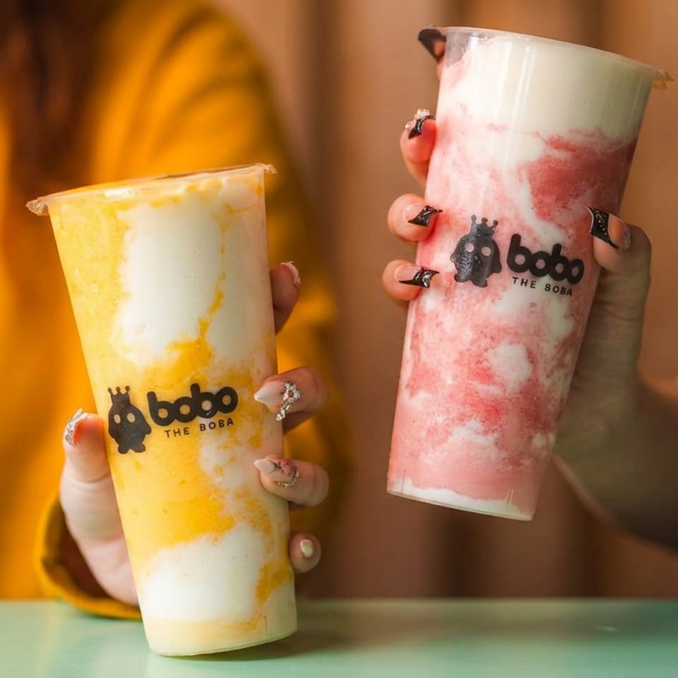 Two hands holding Boba The Boba drinks, one yellow and white, one pink and white.