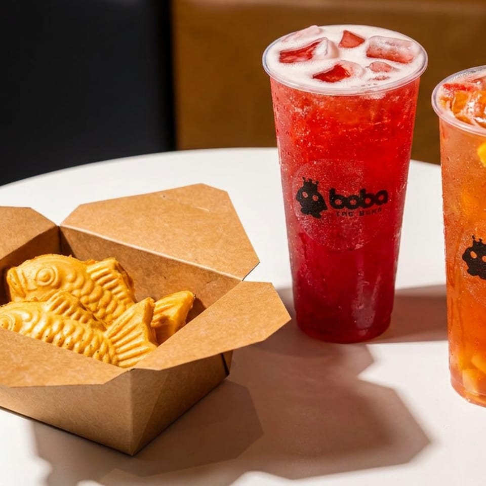 Two Boba The Bann fruit drinks and a box of taiyaki pastries on a white table.