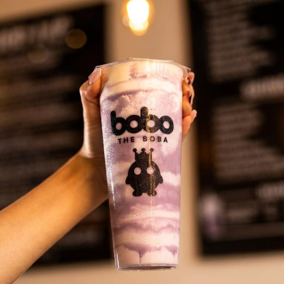 A hand holds up a Bobo The Boba drink, a purple and white swirled beverage with a logo.